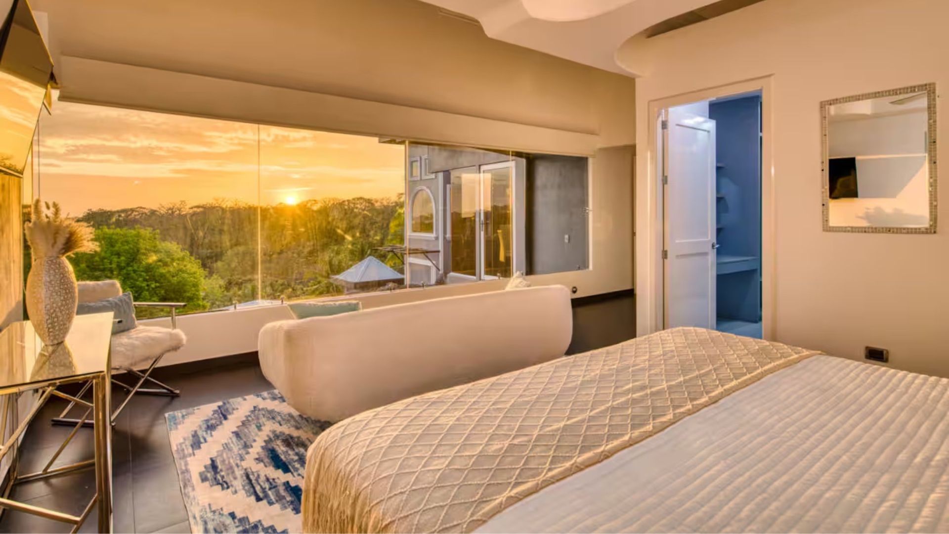 Master bedroom at the Costa Rica retreat villa with floor-to-ceiling windows framing a golden sunset over the jungle
